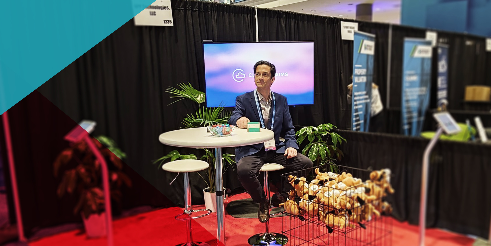 RiskWorld 2025 exhibit hall: Bill Nagle sits at a high-top table branded “Cloud Claims,” beside a wire basket overflowing with “This Is Fine” plush dogs and APPTech materials.
